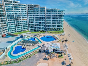 A resort with multiple swimming pools, a beach area, and high-rise buildings in the background.