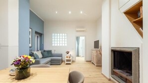 Una sala de estar moderna con un sofá, una mesa de comedor con sillas, una chimenea y un televisor sobre un mueble de madera.