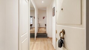 Un pasillo con suelo de madera, paredes blancas y una puerta con picaporte y cerradura de latón.