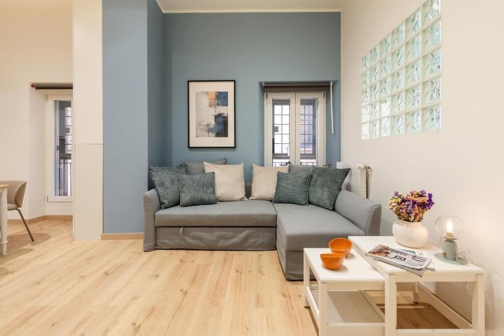 A modern living room with a grey sectional sofa, a white coffee table, and a window with decorative glass panels.