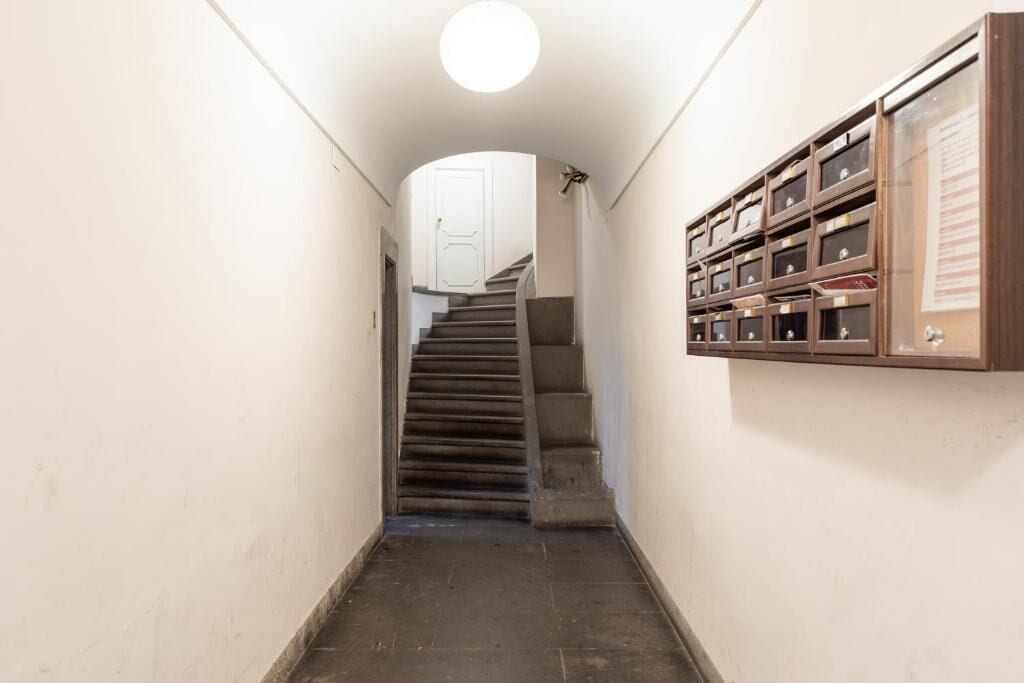 A narrow hallway with a wooden staircase leading to a white door at the end.