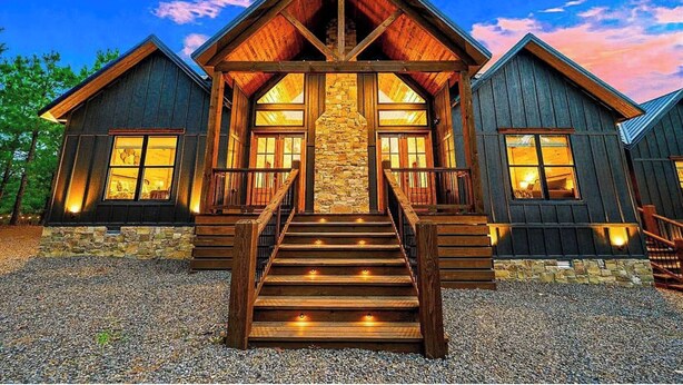A log cabin with a central stone fireplace, wooden stairs, and two attached structures.
