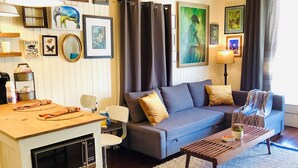 A living room with a sofa, coffee table, and a TV. There are framed pictures on the wall and a lamp on a side table.