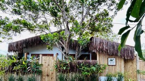 A rustic house with a thatched roof, surrounded by lush greenery and a wooden fence. - 🌴 Casa Preguiça in Corumbau – Comfort and Nature in Southern Bahia 🌊 (Prado)