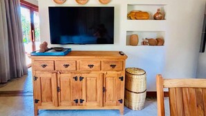 A wooden cabinet with drawers, a television mounted above it, and decorative items on the wall. - 🌴 Casa Preguiça in Corumbau – Comfort and Nature in Southern Bahia 🌊 (Prado)