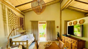 A cozy room with a wooden dining table, a sofa, a TV, and a large window with curtains. - 🌴 Casa Preguiça in Corumbau – Comfort and Nature in Southern Bahia 🌊 (Prado)