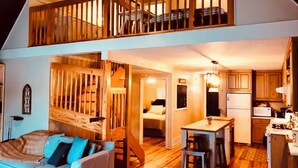 A loft-style apartment with a wooden staircase, a kitchen, a dining area, and a living room with a sofa.
