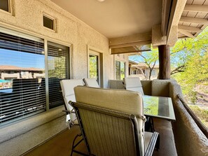 A balcony with a table and chairs, large windows, and a view of buildings and trees.
