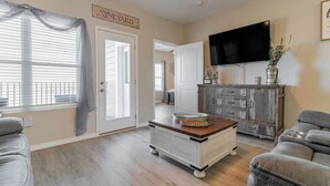 A living room with a television, a vintage sign reading "VINEYARD", a wooden coffee table, and a gray sofa.