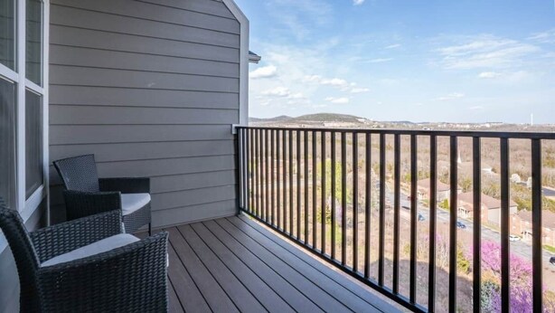 A balcony with a view of a residential area, a chair, and a window.