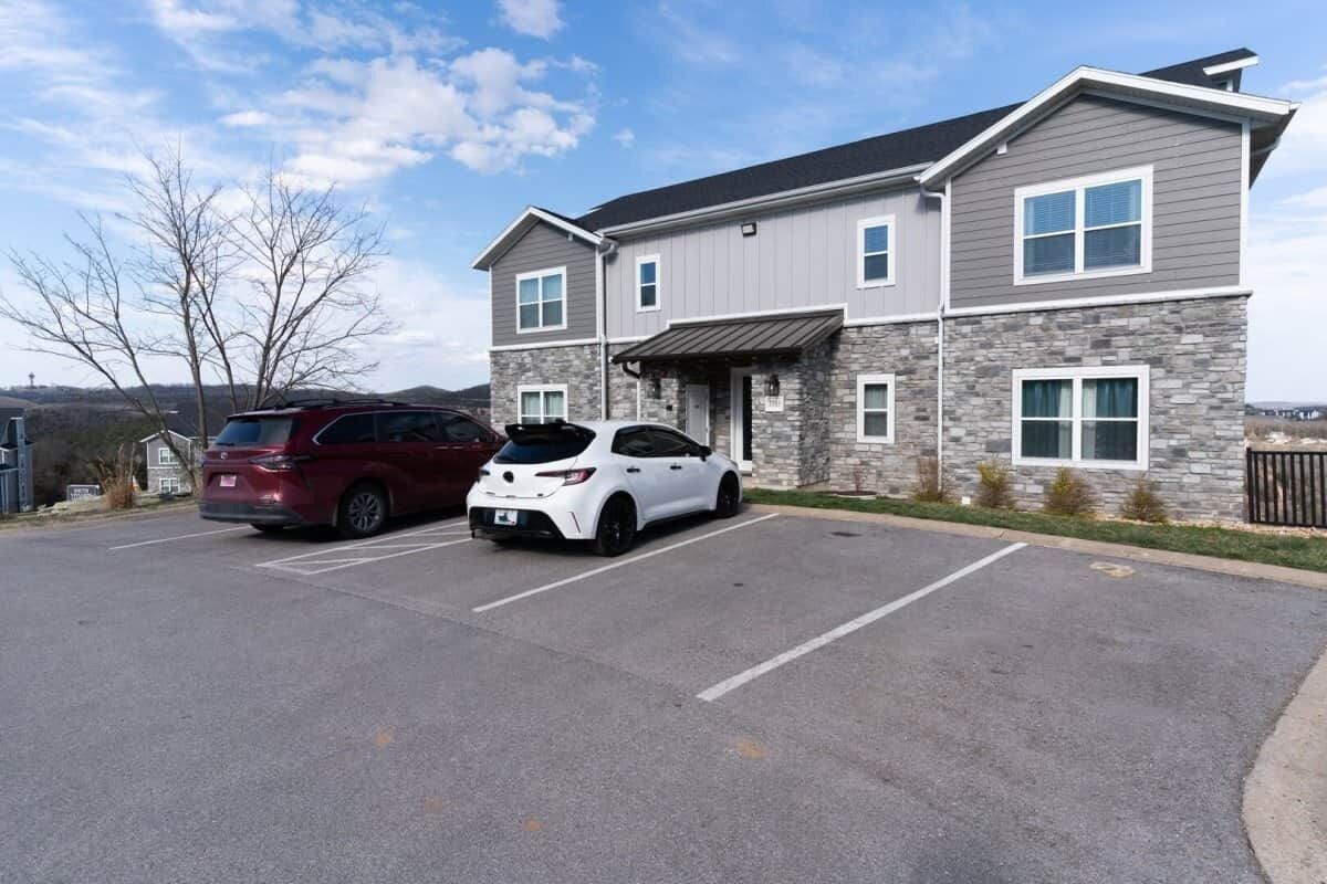 A two-story building with a stone facade and a flat roof. There are two cars parked in front.
