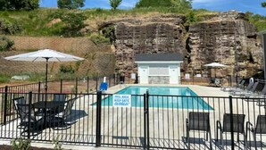 A pool area with a closed gate sign, surrounded by a fence, with lounge chairs and umbrellas.