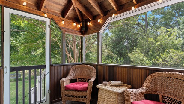 A covered porch with wicker furniture and a view of the surrounding trees. - Heron's Hideaway - A Trusted Guest Favorite for Spacious Comfort! (Chincoteague Island)