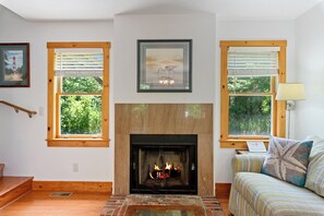 A room with a fireplace, wooden windows, a framed picture, and a couch.