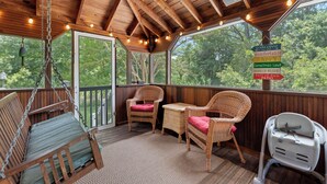 A porch with wicker furniture, a swing, and a sign indicating it's a comfortable and happy place. - Heron's Hideaway - A Trusted Guest Favorite for Spacious Comfort! (Chincoteague Island)