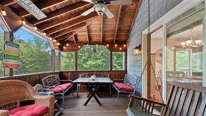 A covered outdoor seating area with wicker furniture and a table, a ceiling fan, and a view of trees. - Heron's Hideaway - A Trusted Guest Favorite for Spacious Comfort! (Chincoteague Island)
