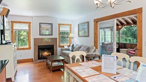 A cozy living room with a fireplace, wooden floors, a dining table with placemats, and large windows with blinds. - Heron's Hideaway - A Trusted Guest Favorite for Spacious Comfort! (Chincoteague Island)