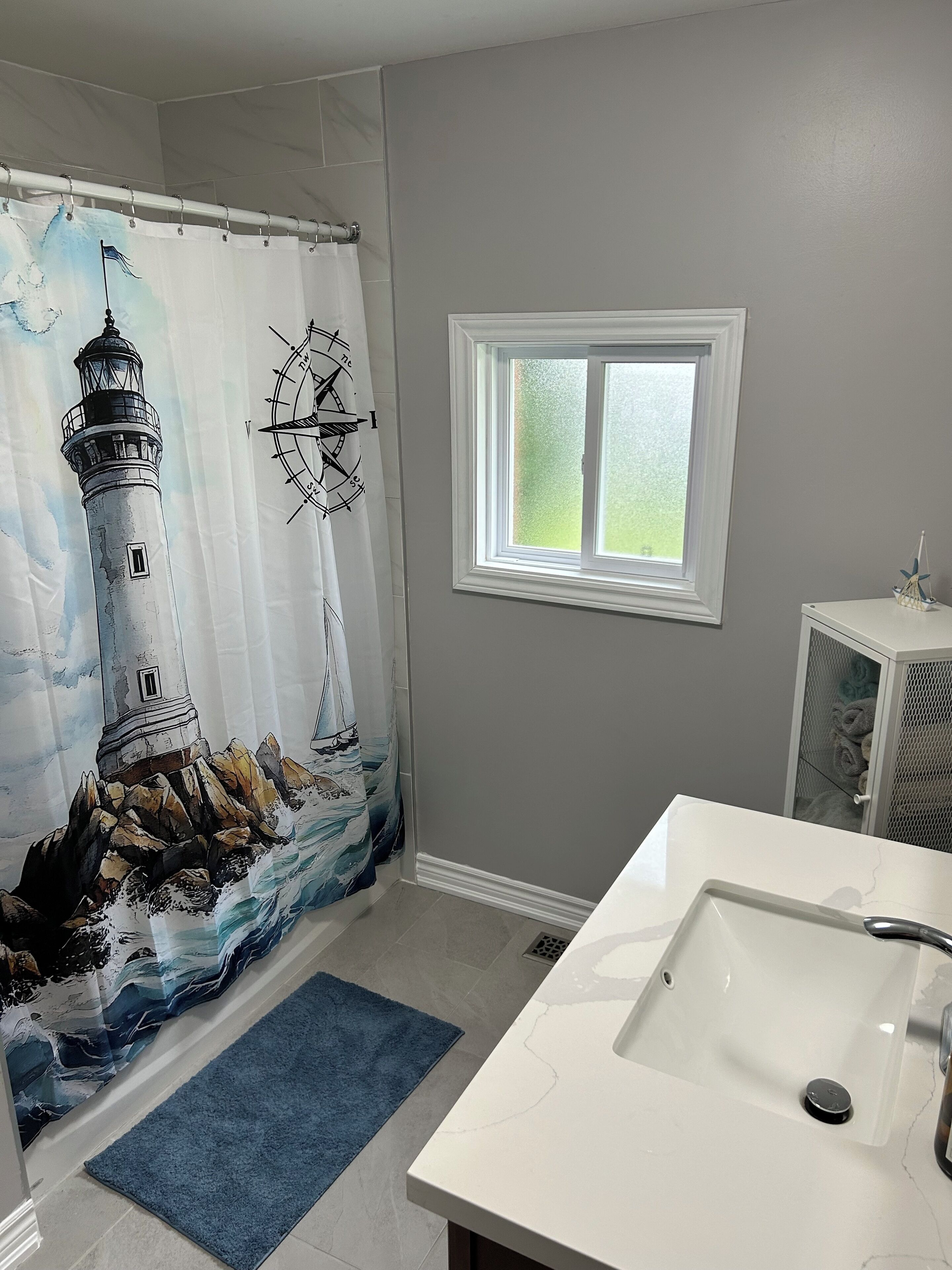 A bathroom with a nautical-themed shower curtain, a window, and a white sink.