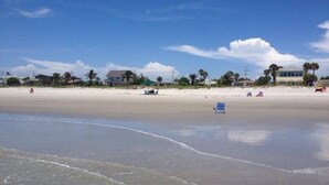 A beach with a clear sky, a few buildings in the background, and a lifeguard tower. - Penguins on the Beach | 2BR Steps to Beach & Downtown w/pool | Unit 4 (Cocoa Beach)