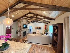A spacious living area with a fireplace, a television, a Christmas tree, and a large wooden ceiling.