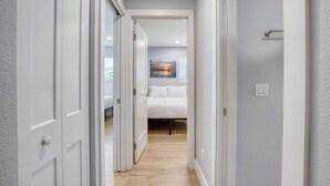 A narrow hallway with a bed at the end, a painting on the wall, and a light switch on the wall. - Drift and Dune Beach, Pet Friendly, Steps to Beach (Ponce Inlet)