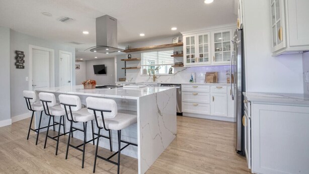 A modern kitchen with a large island, bar stools, white cabinetry, and a built-in oven. - Drift and Dune Beach, Pet Friendly, Steps to Beach (Ponce Inlet)
