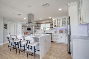 A modern kitchen with a large island, bar stools, white cabinetry, and a built-in oven.