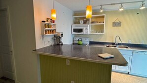 A kitchen with a central island, pendant lighting, and a microwave. - Penguins on the Beach | 2BR Steps to Beach & Downtown w/pool | Unit 2 (Cocoa Beach)