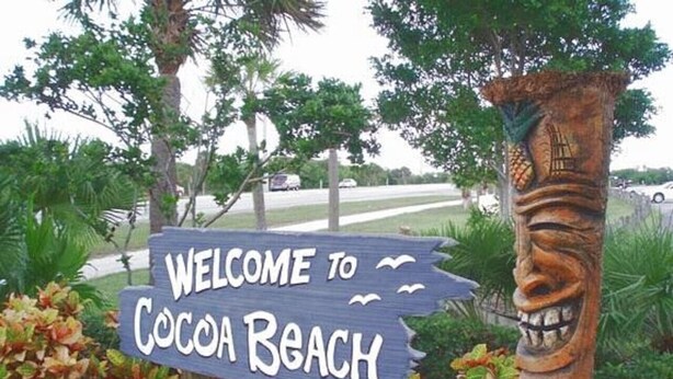 A welcome sign for Cocoa Beach with a wooden structure and a carved face. - Penguins on the Beach | 2BR Steps to Beach & Downtown w/pool | Unit 2 (Cocoa Beach)