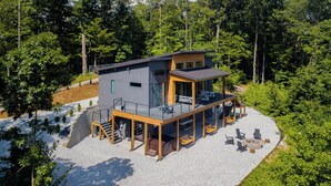 A modern cabin with a deck, surrounded by trees.