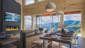 A modern interior with a fireplace, seating area, dining table, and large windows offering mountain views.