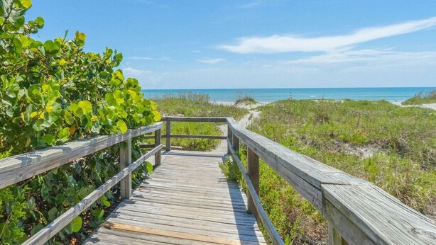 Une promenade en bois qui mène à une plage, avec un ciel dégagé.