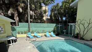 Une piscine avec des chaises longues, une table et une cl ôture verte.