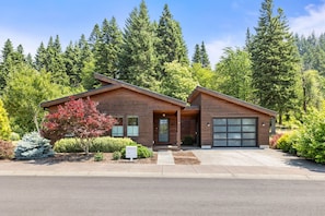 A two-story house with a garage, surrounded by dense forest. - Modern Gorge Retreat • Hot Tub • Mountain Views (Cascade Locks)