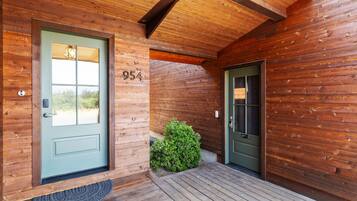 A wooden cabin with a green door, a number '954' on the wall, and a small green bush in front.