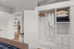 A bedroom with a bed, a white wardrobe, and a closet with hanging clothes and folded items.