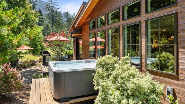 A wooden house with large windows, a hot tub, and outdoor seating. - Modern Gorge Retreat • Hot Tub • Mountain Views (Cascade Locks)