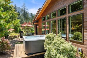 Ein Holzhaus mit großen Fenstern, einem Whirlpool und Sitzgelegenheiten im Freien.