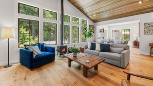 A spacious living room with a fireplace, large windows, and a high ceiling. - Modern Gorge Retreat • Hot Tub • Mountain Views (Cascade Locks)