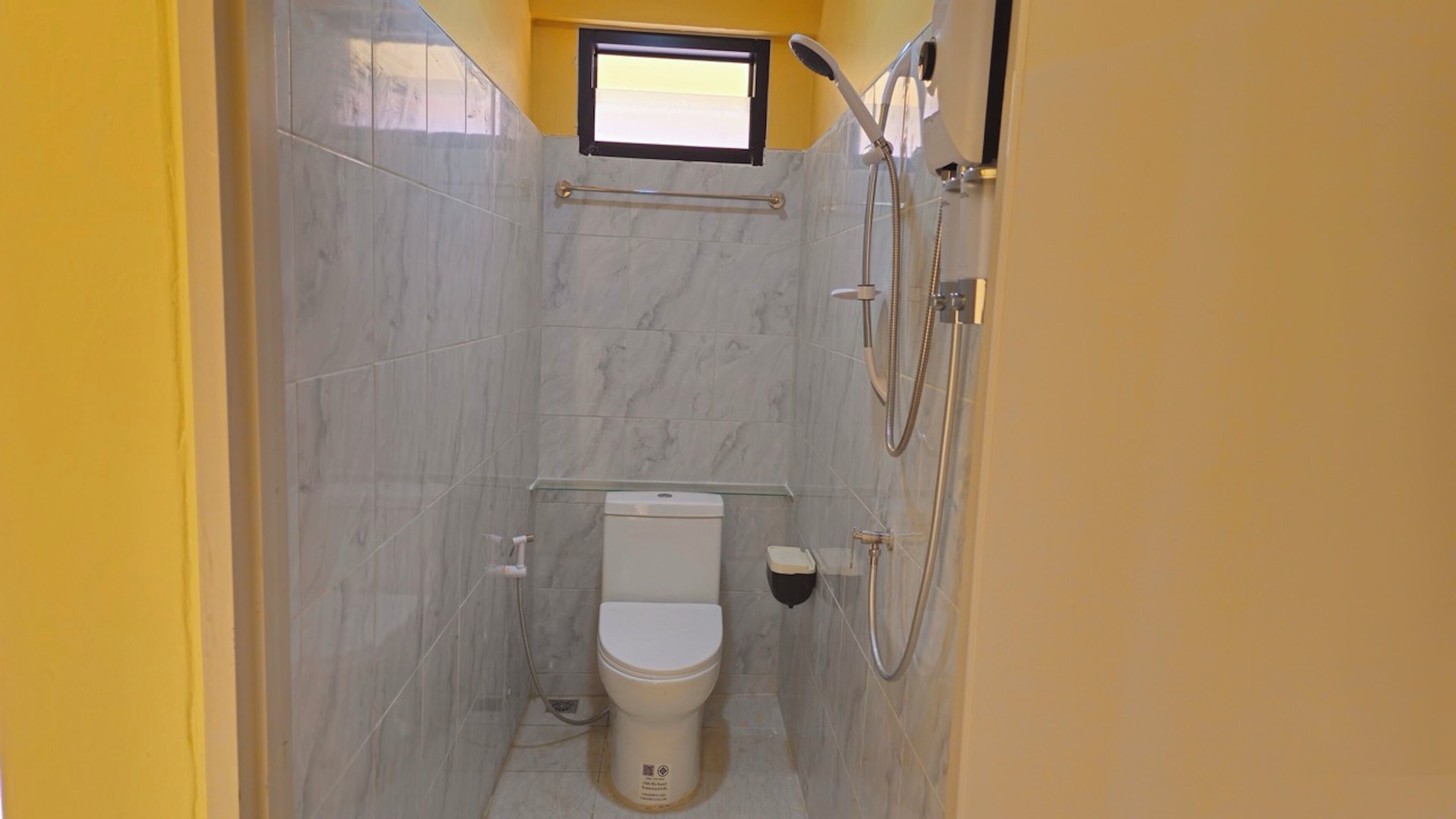 A small, compact bathroom with a toilet, a shower, and a window.