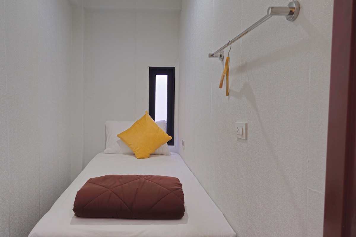 A narrow, single-bed room with white walls, a window, and a door.