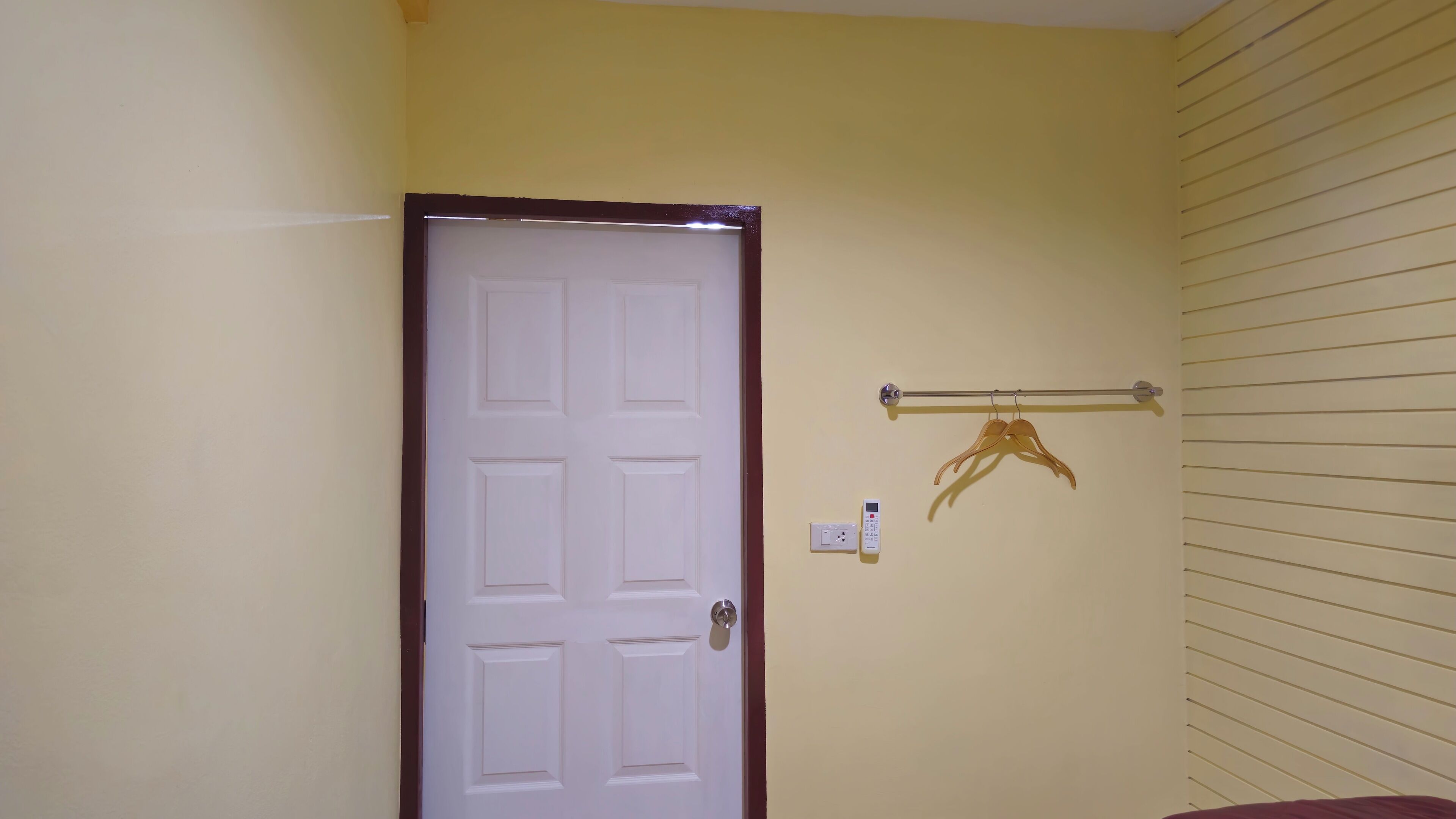 Une pièce avec une porte blanche, un porte-serviettes muni de crochets et un thermostat fixé au mur.