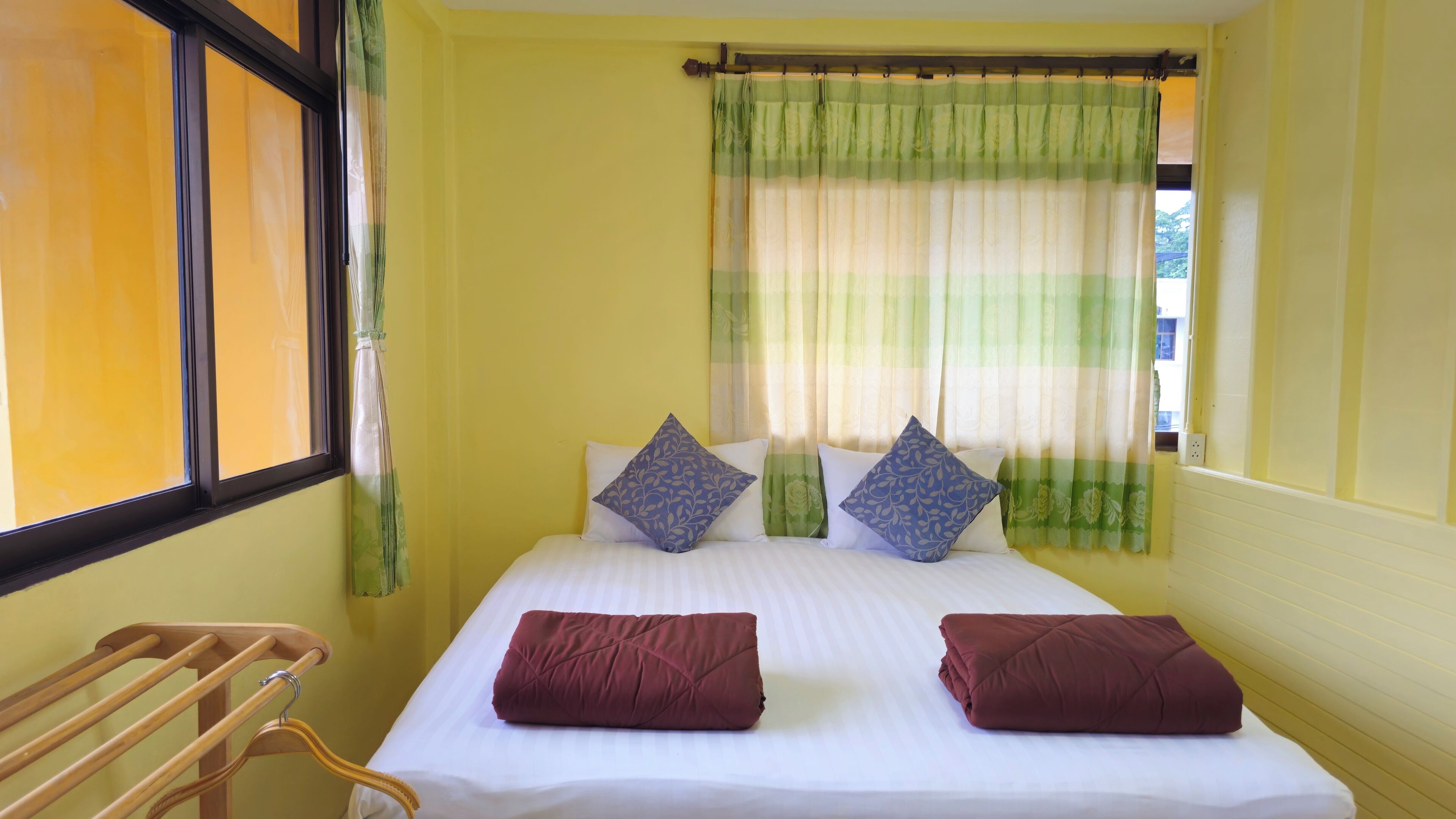 A room with a bed, two pillows, a window with curtains, and a wooden towel rack.
