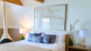 Une chambre à coucher avec un grand lit, une table de chevet, une lampe, un tableau accroché au mur et une poutre en bois au plafond.