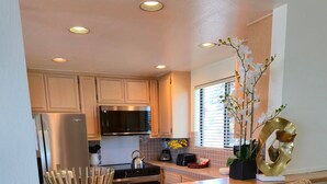 A kitchen with wooden cabinets, a stainless steel refrigerator, a microwave, and a sink. There are two wicker chairs at a wooden bar counter. - Tahoe Vista Inn Suite 7 (Tahoe Vista)