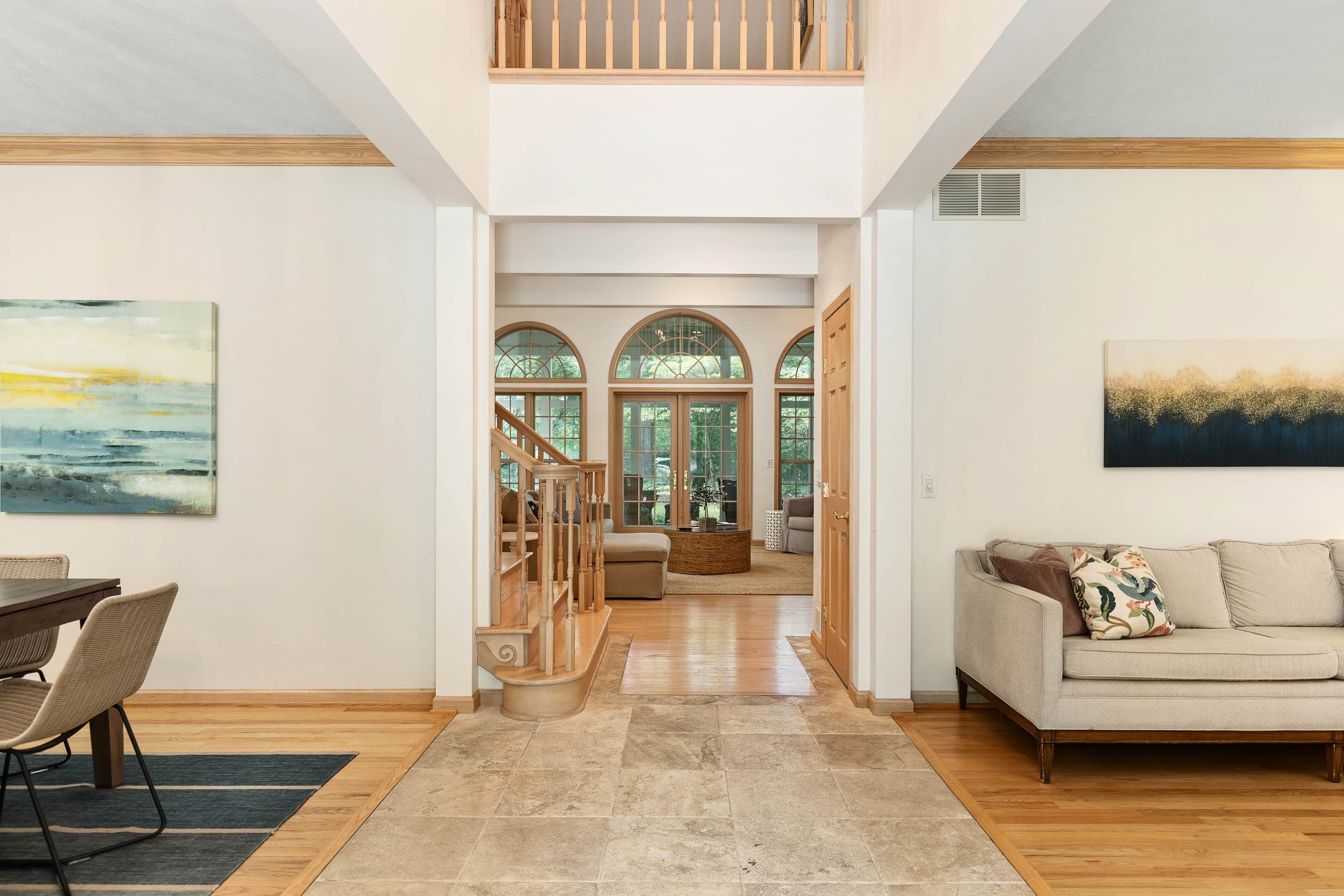 A spacious interior with a wooden staircase, a beige sofa, and a dining area with chairs.