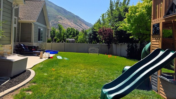 Ein Garten mit einer Rutsche, einer Terrasse mit Sitzgelegenheit und einem Berg im Hintergrund.