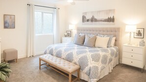 Ein Schlafzimmer mit einem großen Bett, einer Bank, einem Nachttisch, einem Deckenventilator und einem Fenster mit Vorhängen.