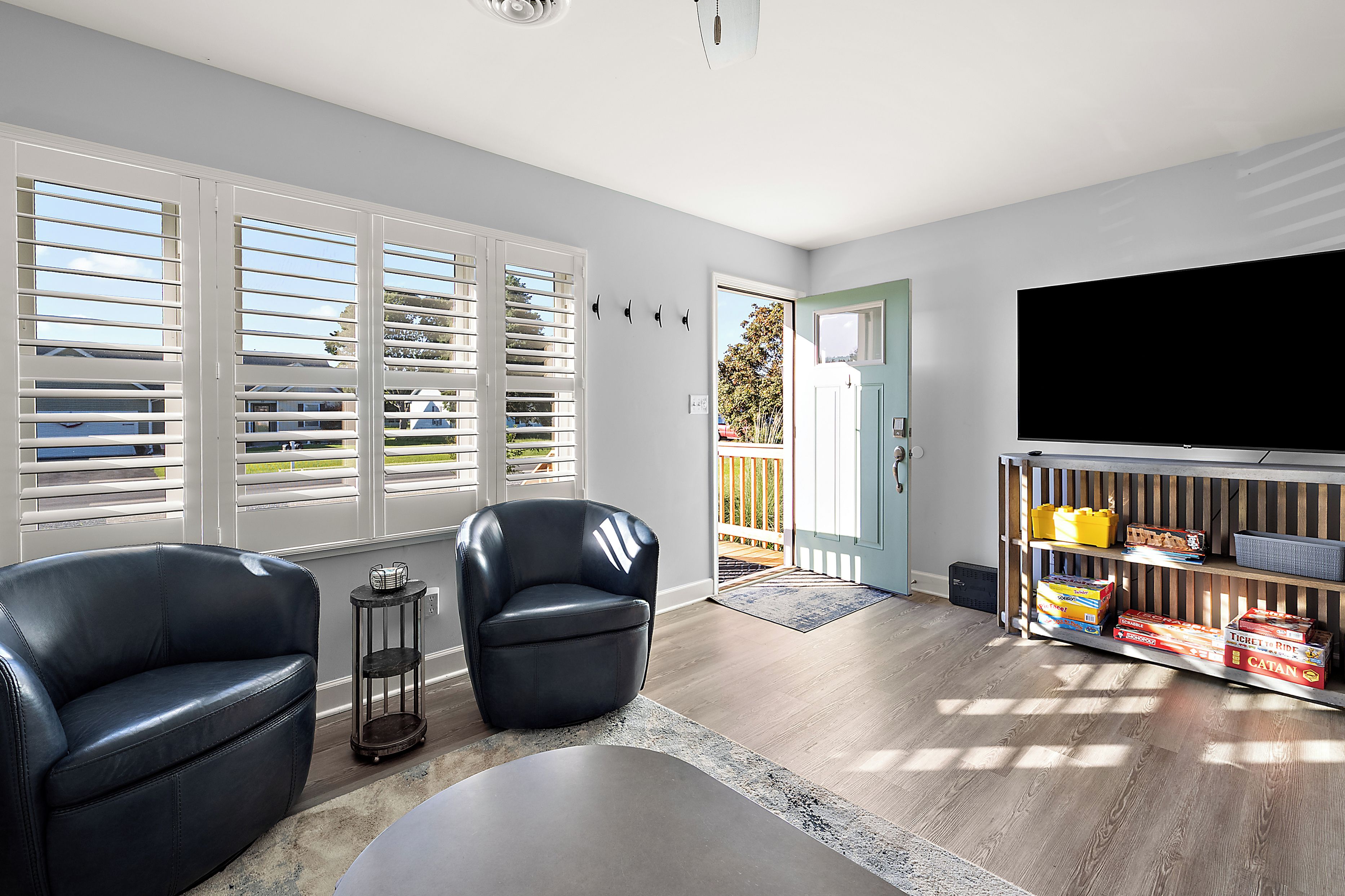 A modern living room with a flat-screen TV, two leather chairs, a coffee table, and a wooden shelf with board games.