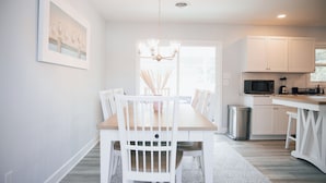 A modern kitchen with white cabinetry, a dining table with chairs, and a chandelier. - 4BR Beach House Sleeps 12/Screened Porch/Parking for 6 cars /Rehoboth (Rehoboth Beach)